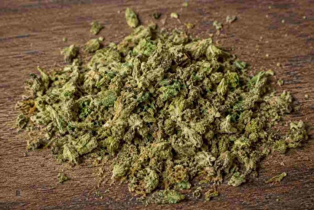 Pile of loose shake weed with visible trichomes on a wooden table