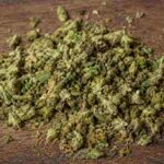 Pile of loose shake weed with visible trichomes on a wooden table