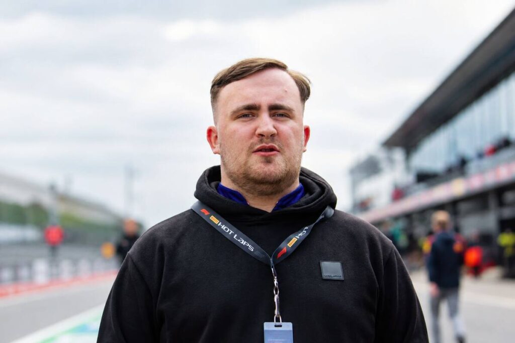 luke littler net worth: Luke Littler standing outdoors wearing a black hoodie and event lanyard.